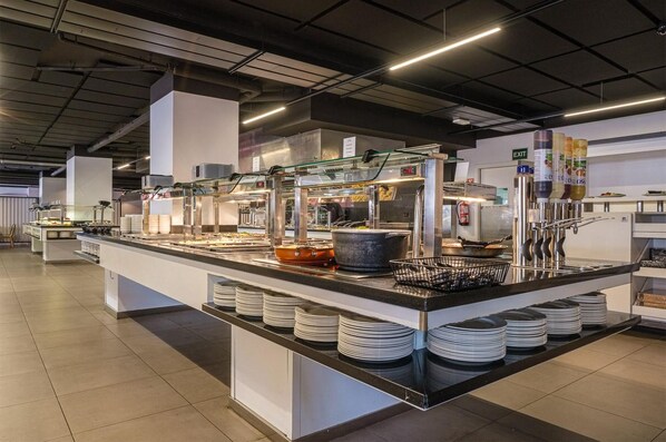 A buffet setup with multiple food stations, a glass display case, and a digital clock. - Estival Park Almaris (Vila-Seca)