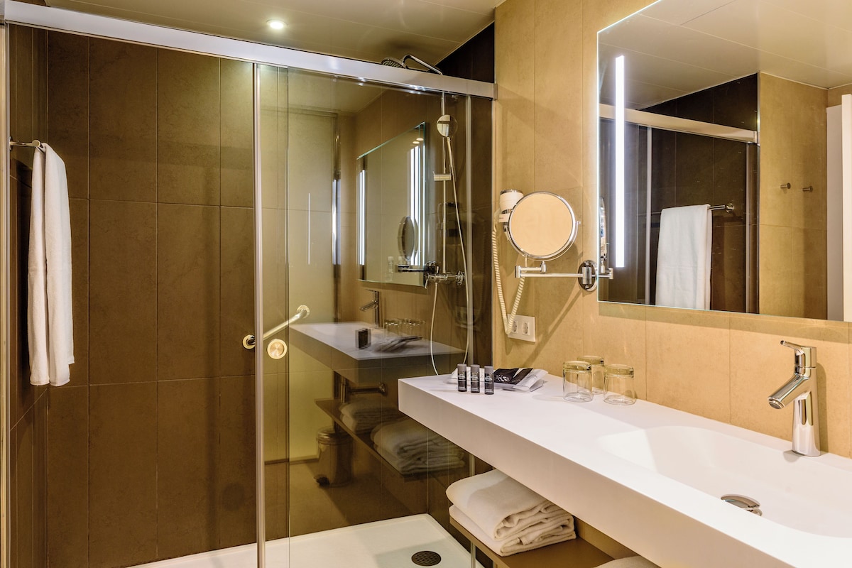 Un baño moderno con ducha de vidrio, un lavabo blanco y un espejo grande.
