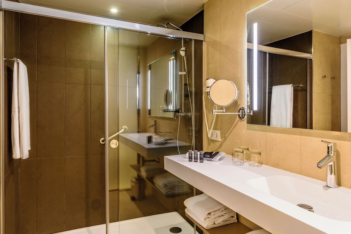 Un baño moderno con ducha de vidrio, un lavabo blanco y un espejo grande.