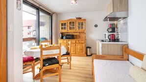 A compact room with a bed, a dining table with chairs, a kitchenette with a microwave and coffee maker, and a sliding glass door to the outside.