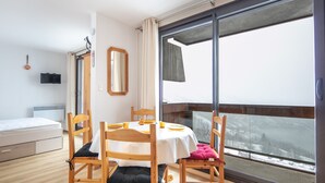 A hotel room with a large window, a bed, a table with chairs, and a mirror.