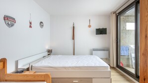 A bedroom with a bed, a wooden chair, a TV, and a sliding glass door.