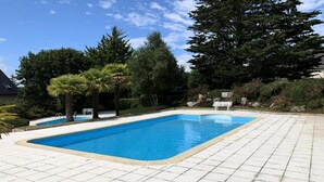 Una piscina rectangular con un borde empedrado, rodeada de diversos árboles y arbustos.