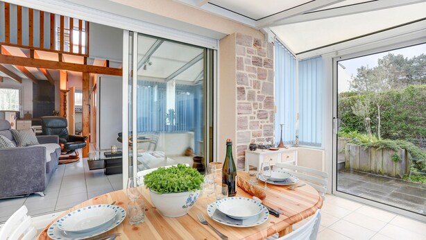Un comedor con una mesa de madera dispuesta para cuatro personas, un tazón de ensalada verde y una botella de vino.