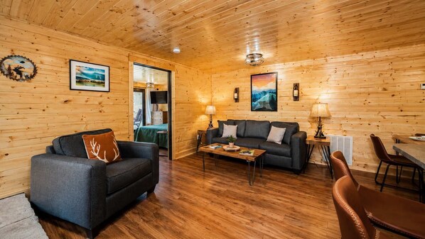 Ein gemütliches Zimmer mit Holzwänden und Holzböden, einer Couch, einem Couchtisch und einer Essecke.