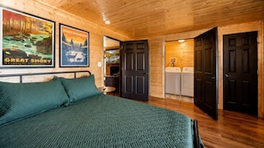 A wooden cabin interior with a bed, a washing machine, and a door leading to another room. - Mountain Views at Dolly's Castle Unit 5 (Sevierville)