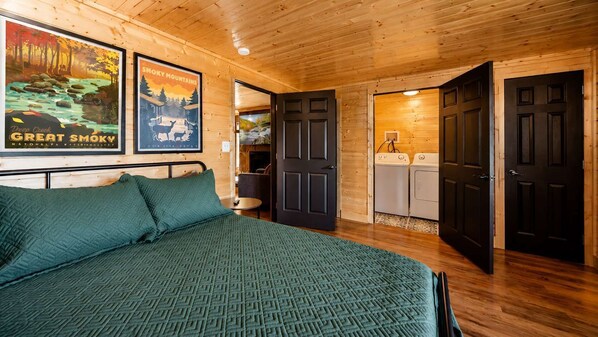 L’intérieur d’une cabane en bois comprend un lit, un lave-linge et une porte qui donne sur une autre pièce.