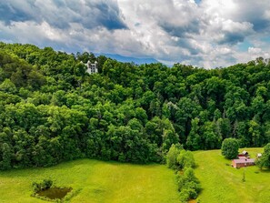 A lush green landscape with a white building on a hill and a red-roofed structure in the foreground. - Mountain Views at Dolly's Castle Unit 5 (Sevierville)