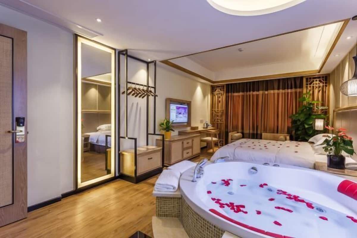 Une chambre d’hôtel moderne dotée d’un grand lit, d’un coin salon séparé, d’un dressing et d’une grande baignoire remplie de pétales de rose.
