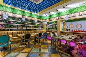A restaurant with a blue ceiling, green wall decorations, and a variety of seating arrangements including tables and chairs. - Yun Jin Bo Li Hotel (Tongxiang)