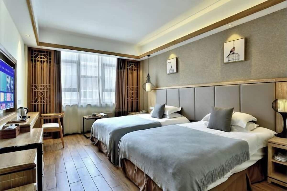 Une chambre d’hôtel avec deux lits, un bureau, une chaise, une télévision et une fenêtre avec des rideaux.