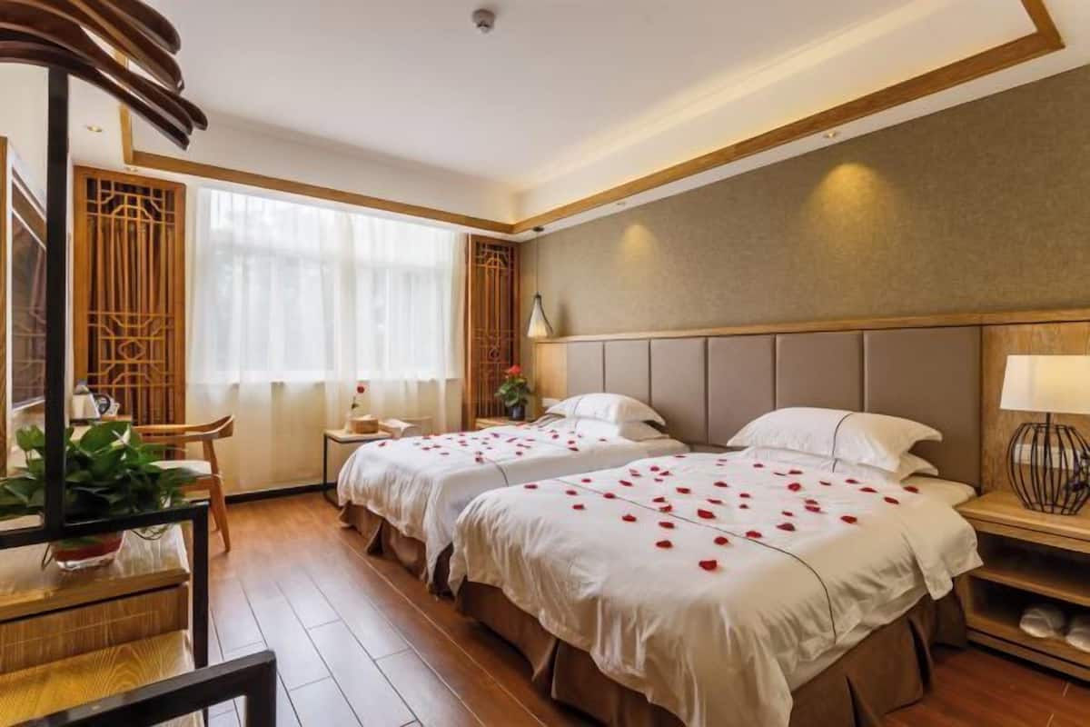 Une chambre d’hôtel avec deux lits, un plancher en bois, une grande fenêtre avec des rideaux et un paravent décoratif de style traditionnel.