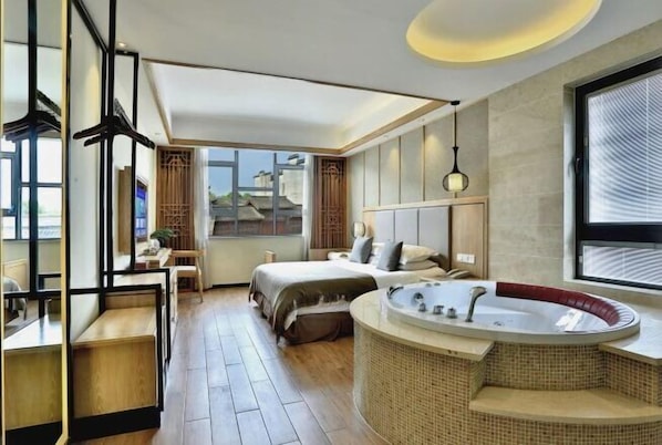 A modern hotel room with a large bed, a curved bathtub, and a view of the city.