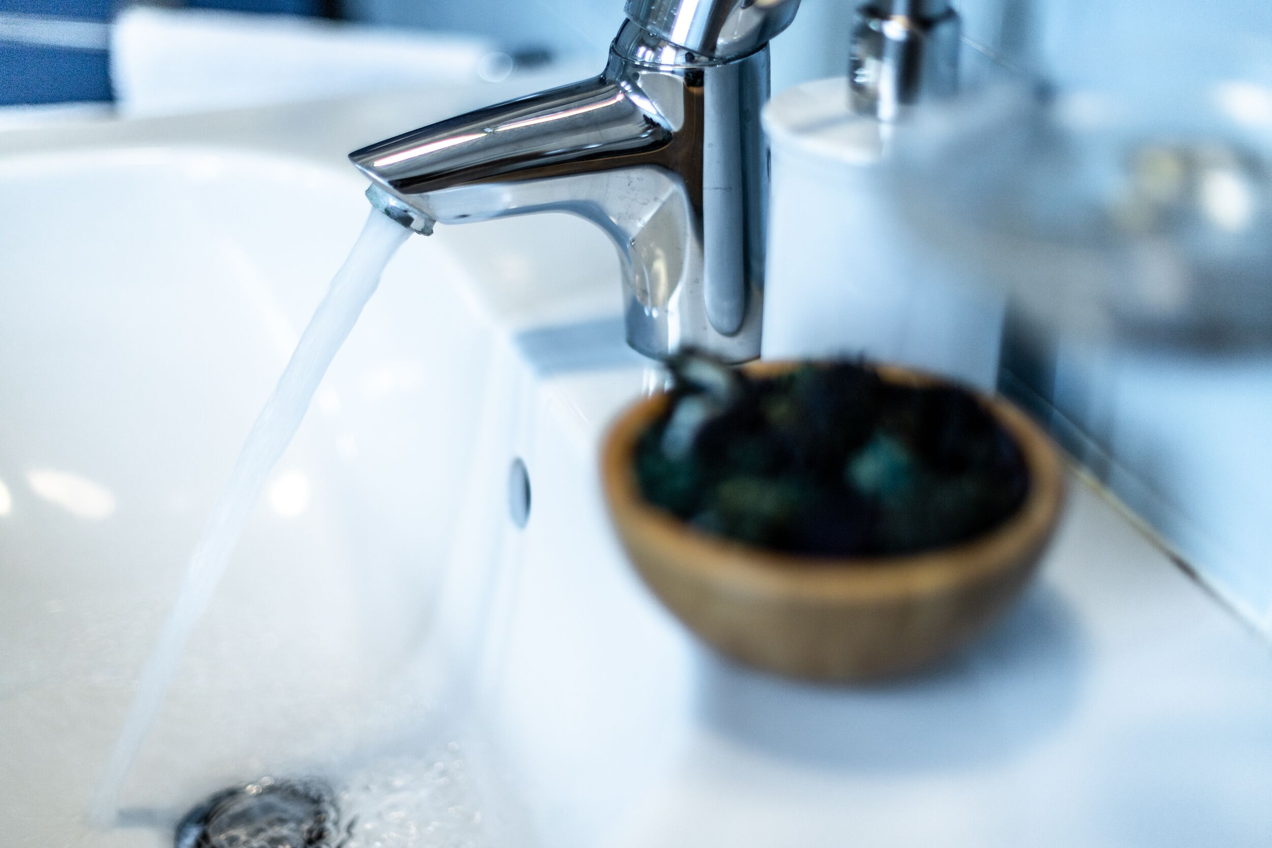 A bathroom sink with running water and a wooden soap dish.