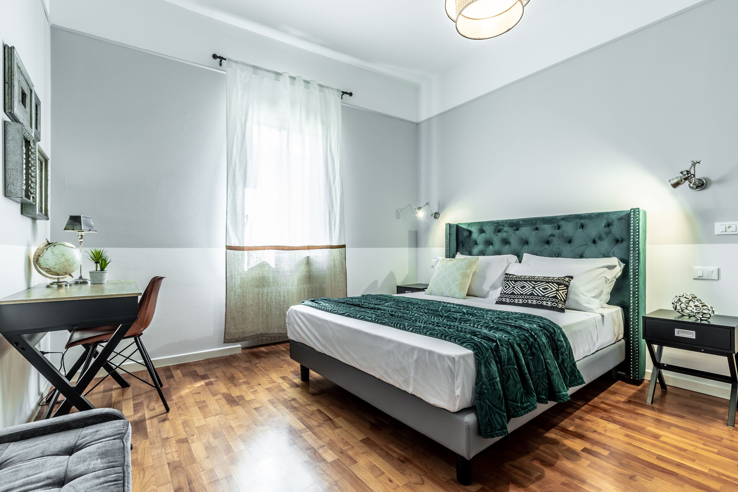 A bedroom with a bed, desk, chair, and a window with curtains.