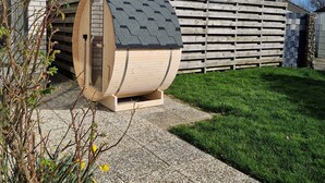 Una estructura en forma de barril de madera con techo inclinado, chimenea de piedra y cerca de madera en un entorno residencial.