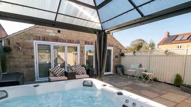 A hot tub in a covered outdoor area with stone walls and a patio. - Garthgate Holiday Lodge (Malton)