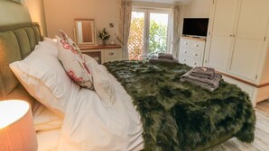 A bedroom with a bed, a dresser, a TV, and a window with a view of greenery. - Garthgate Holiday Lodge (Malton)