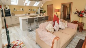 A modern living room with a sofa, a dining area with a kitchen in the background, and a large window providing natural light. - Garthgate Holiday Lodge (Malton)