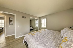 A bedroom with a large bed, a dresser, and a mirror. There are two windows and a door leading to another room. - The Harold House (Olathe)