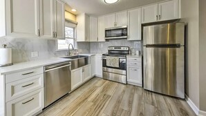 A modern kitchen with white cabinets, stainless steel appliances, and a wooden floor. - The Harold House  (Olathe)