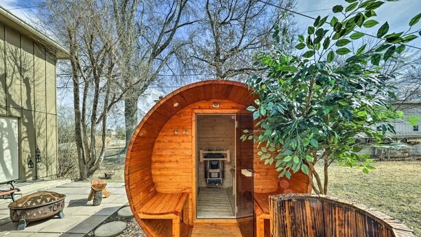 A wooden structure with a bench and a small table, surrounded by trees and a building. - The Harold House  (Olathe)