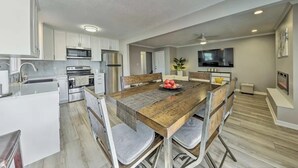 A modern kitchen with white cabinets, stainless steel appliances, and a wooden dining table with chairs. - The Harold House  (Olathe)