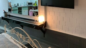 Een moderne kamer met een bed, een televisie die aan een bakstenen muur bevestigd is, en een keukenhoek die in de spiegel zichtbaar is.