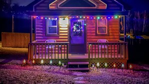 Eine Blockhütte mit Veranda, beleuchtet durch Lichterketten und ein Neonzeichen.
