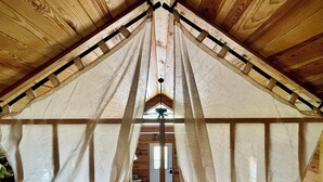 Ein schrägwangiges Schlafzimmer im Dachgeschoss mit Holzbalkendecke und kleinem Fenster.