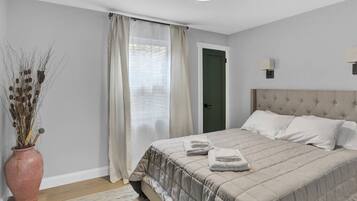 Une chambre à coucher avec un lit, des rideaux, un vase contenant des plantes séchées et une porte.