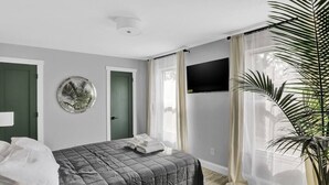 A bedroom with a bed, a wall-mounted TV, a door, and a large window with sheer curtains. - Luxury Apartment In Lakewood (Lakewood)