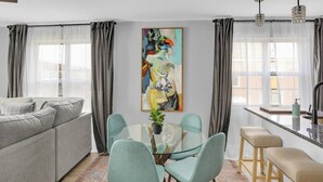 A modern living room with a grey sofa, a glass dining table with four chairs, and a large abstract painting on the wall. - Luxury Apartment In Lakewood (Lakewood)