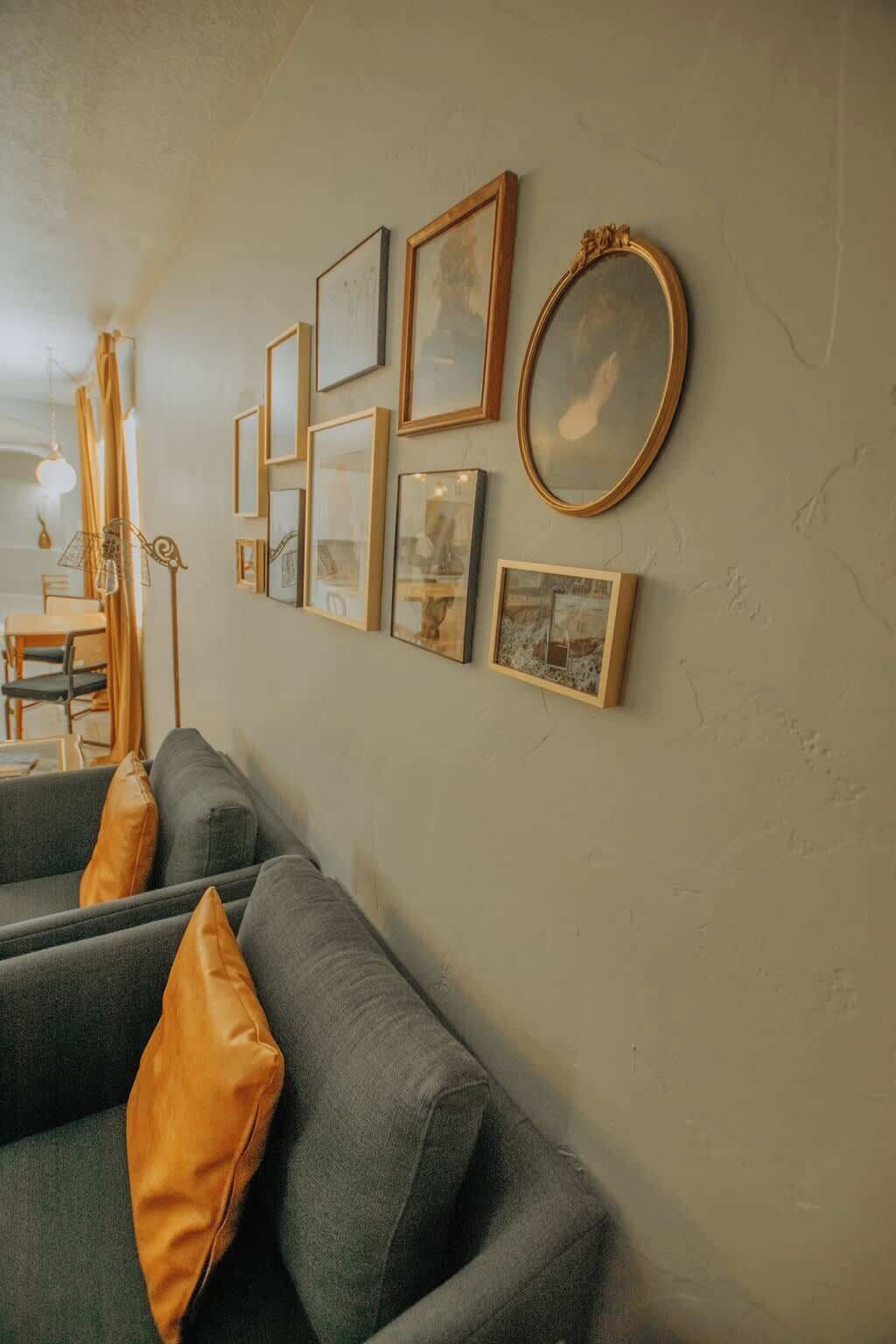 A living room with a grey sofa, multiple framed pictures, and a large mirror on the wall.