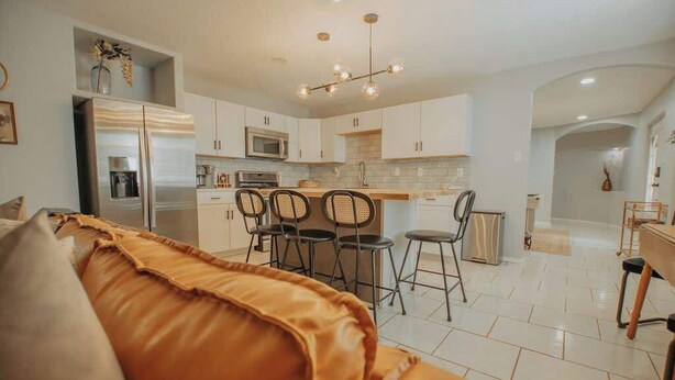 A modern kitchen with white cabinets, a stainless steel refrigerator, and a dining area with four chairs.