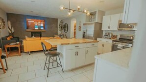 A modern kitchen with white cabinets, a wooden island, and a dining area with a sofa and chairs.