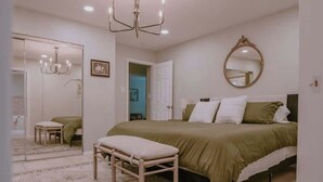 A bedroom with a bed, bench, chandelier, and a mirror on the wall.