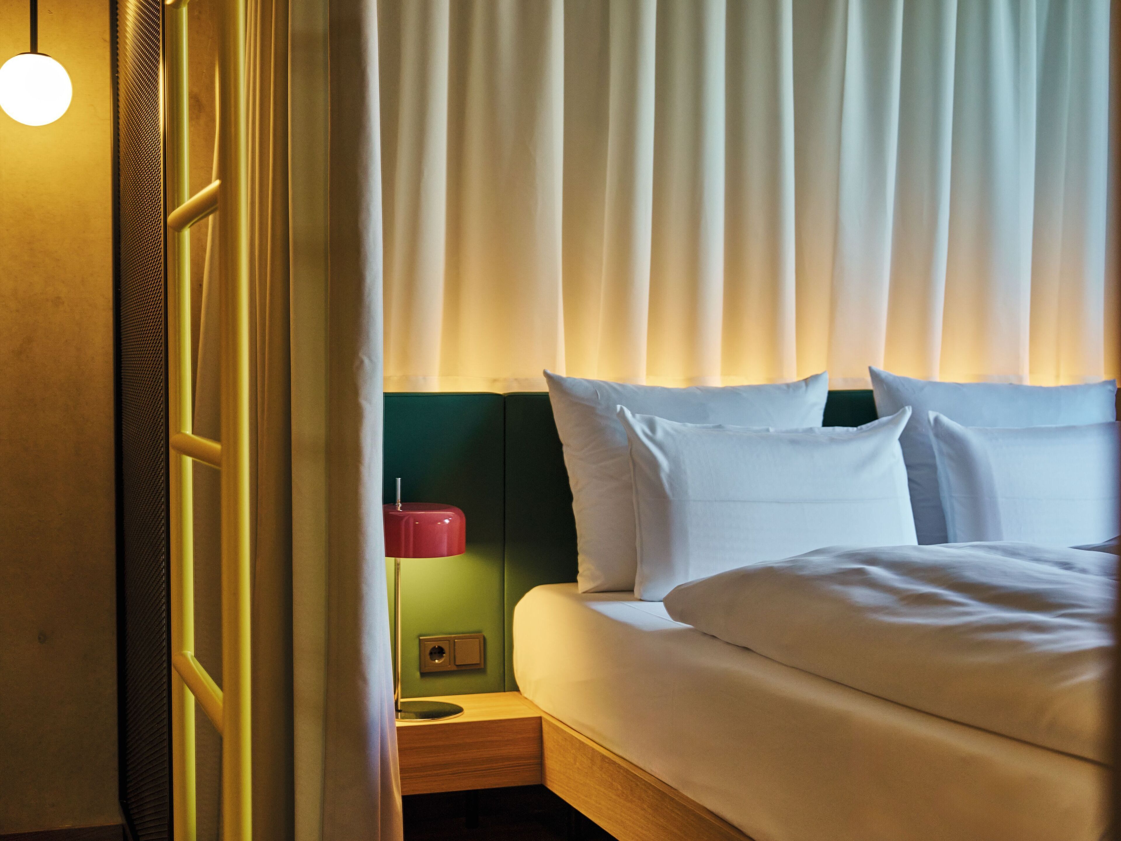 Une chambre d’hôtel avec un lit, une table de chevet, une lampe rouge et un mur vert.