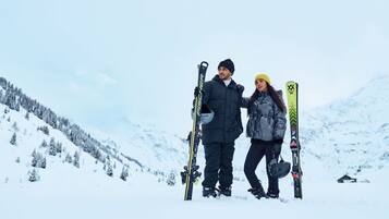 Two people standing on a snowy mountain with skis, surrounded by snow-covered trees and a clear sky.