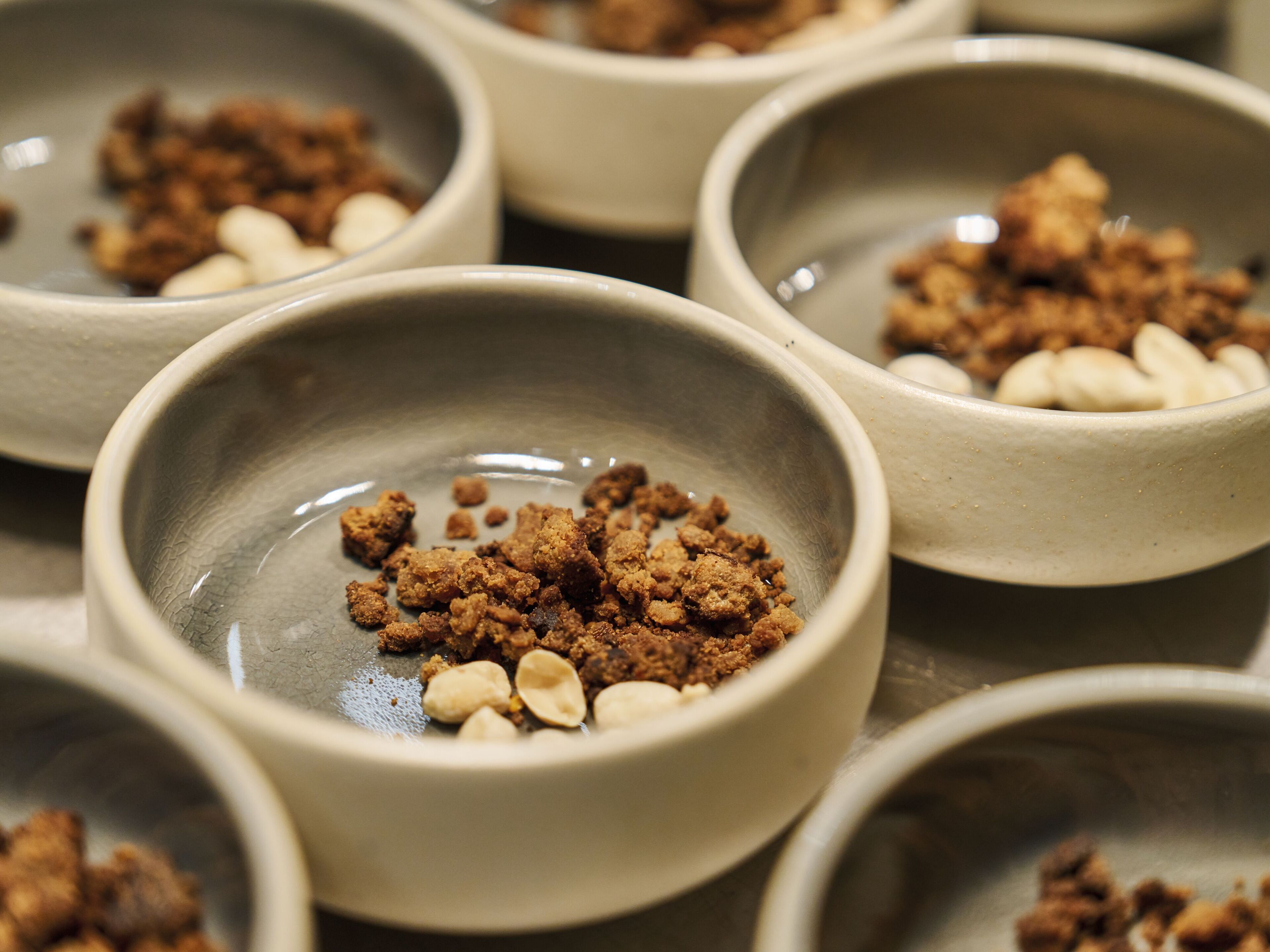 Multiple bowls containing a mixture of brown crumbs and white nuts.