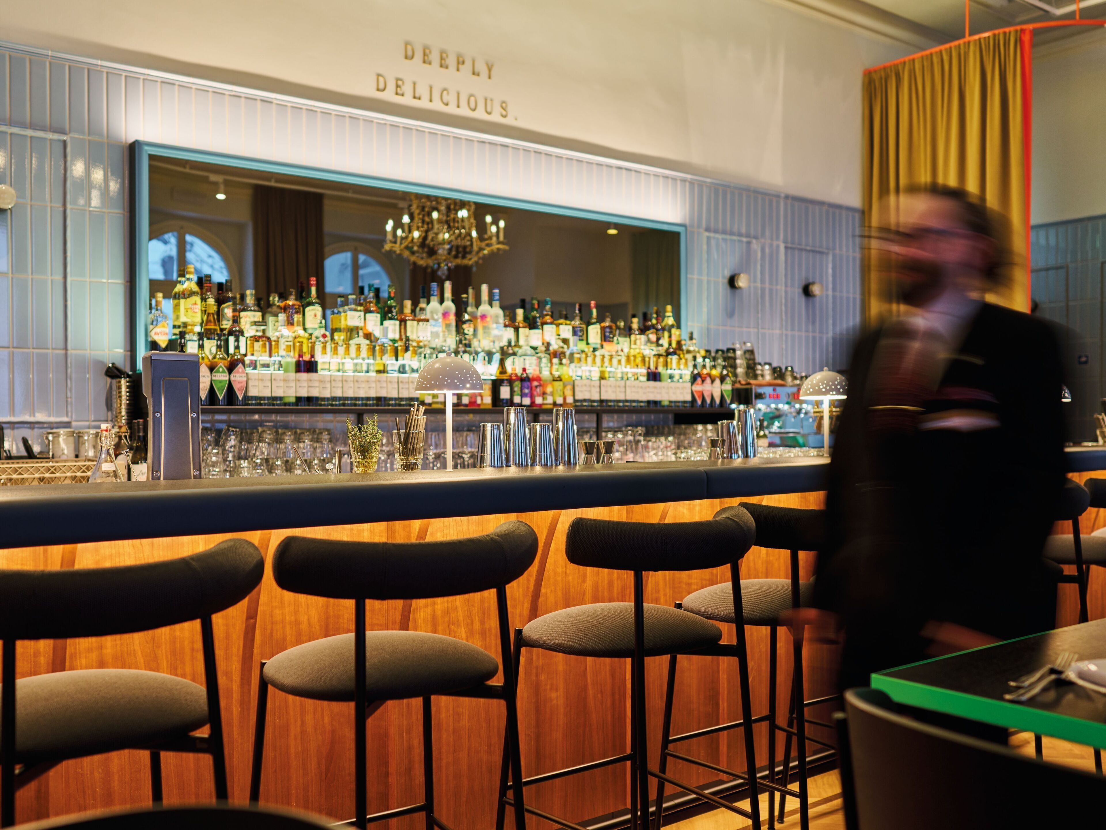 A bar area with stools, a bar counter, and a variety of bottles and glasses.