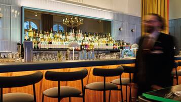 Uma área de bar com banquetas, balcão e diversos copos e garrafas.