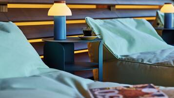 Une chambre d’hôtel moderne avec une tête de lit en bois, une petite table ronde avec une lampe et un magazine posé sur le lit.