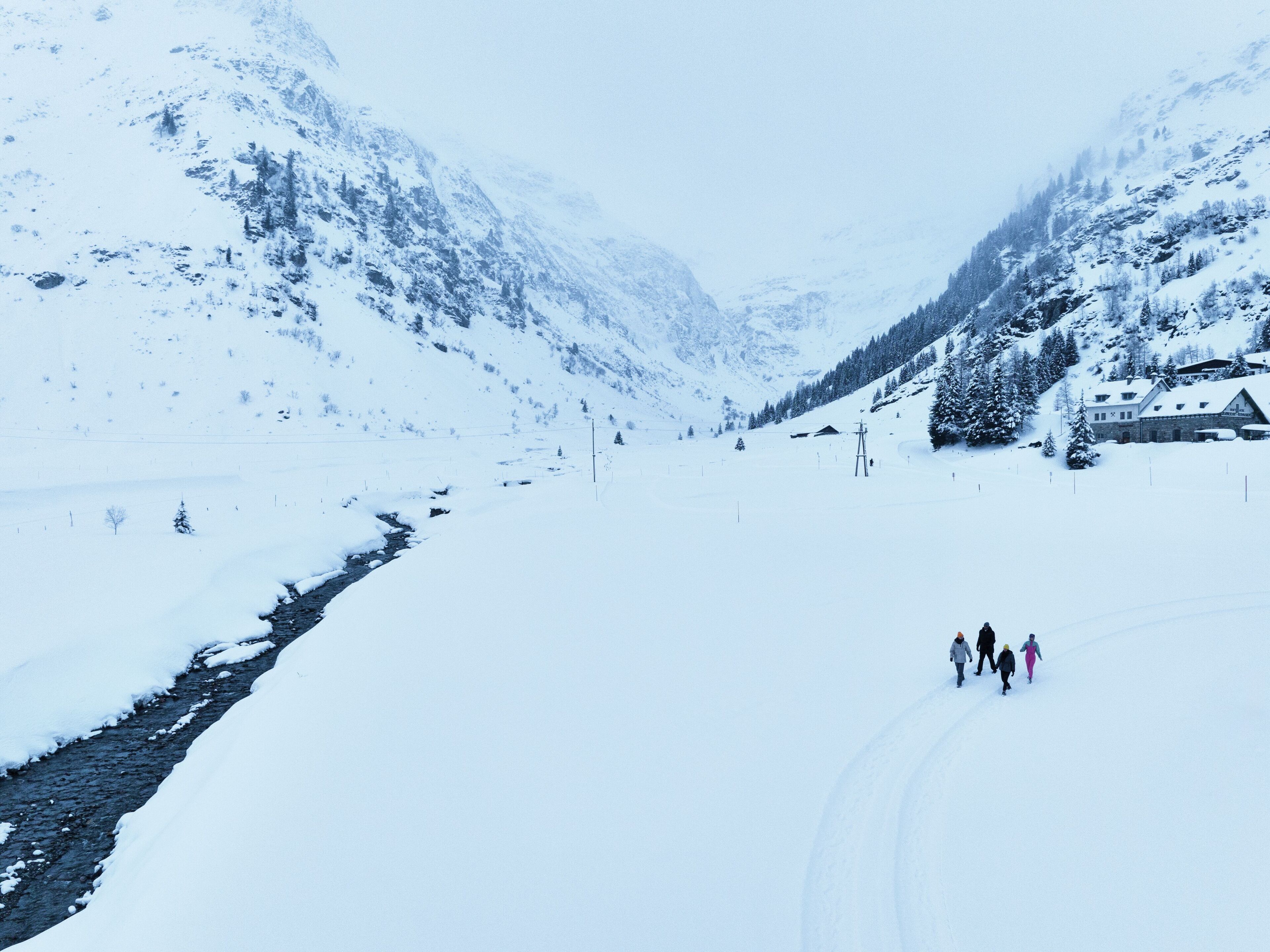 A snow-covered mountain landscape with a building and a few people walking.