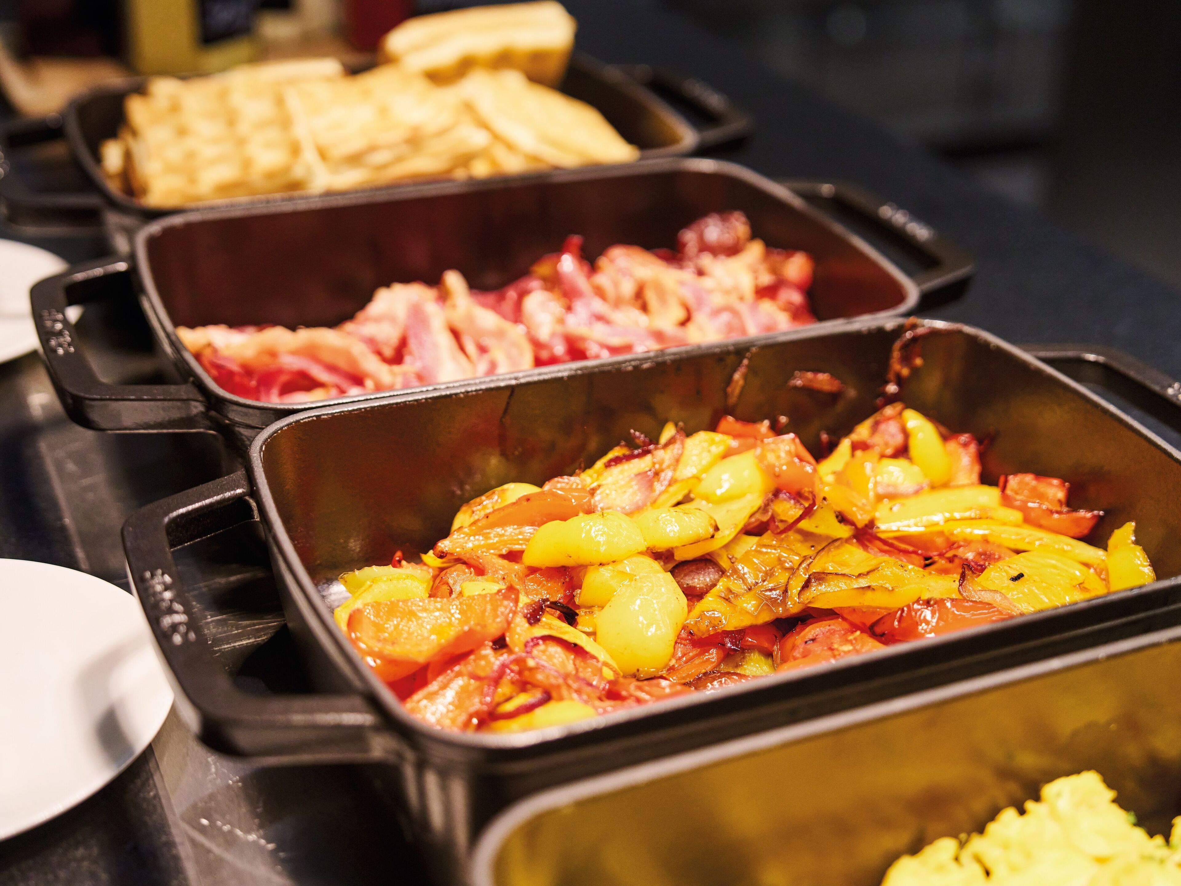Un bufé con diversos platos, entre ellos, patatas, tocino y huevos revueltos.