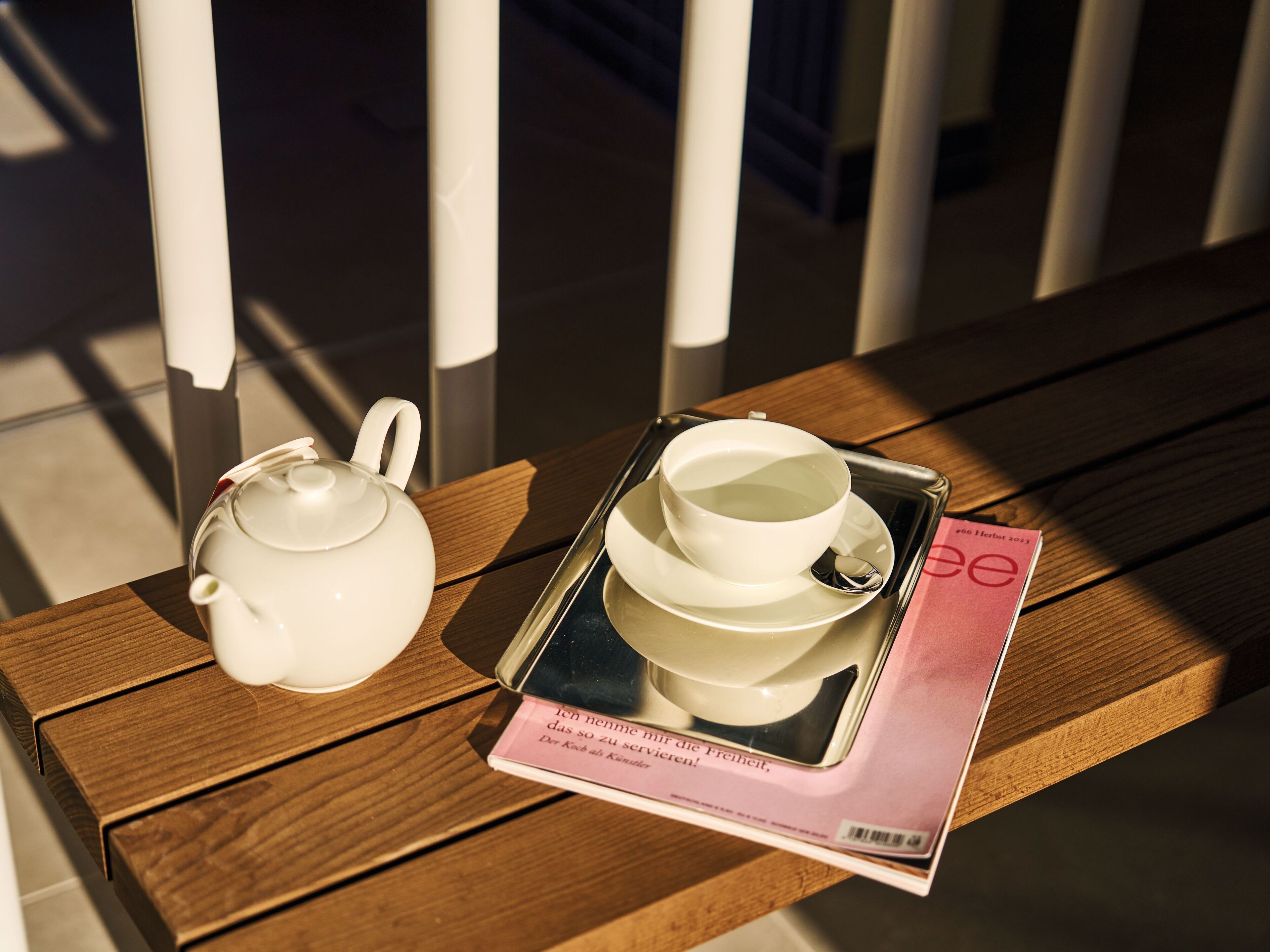 Ein Holztisch mit einem Teekessel, einer Tasse, einem Untertasse und einer Zeitschrift.
