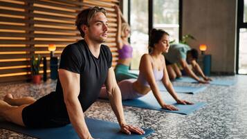 Una lezione di yoga in una stanza con pavimento decorato e listelli di legno alle pareti.
