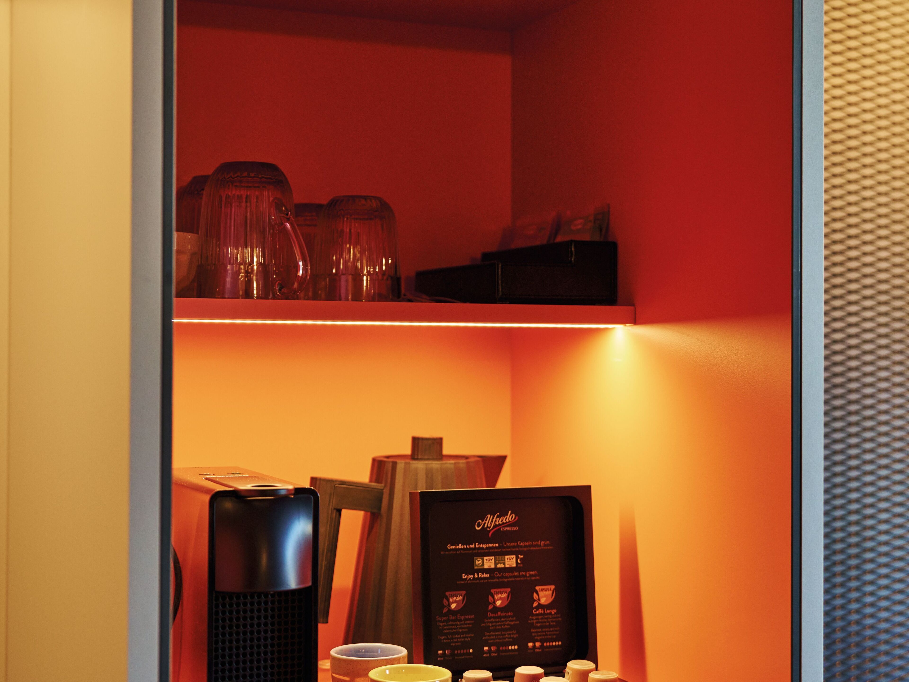 Una cafetera, tazas y un menú en una habitación con paredes rojas.