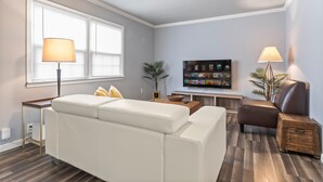 Un salon moderne avec un canapé blanc, un fauteuil en cuir marron et un téléviseur à écran plat posé sur un meuble en bois.