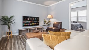 Un salon moderne avec un téléviseur à écran plat, un fauteuil en cuir, un canapé blanc et une petite table basse en bois.